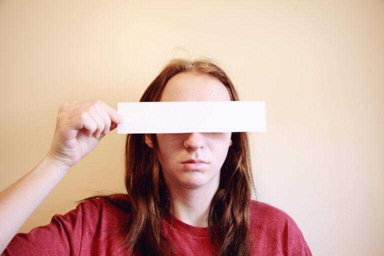 Person holding blank rectangle of paper over eyes.
