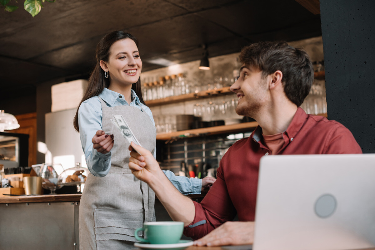 young man paying cash at a coffee shop to a young waitress