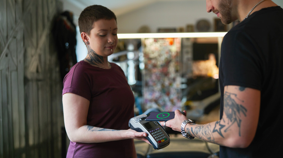 young man paying with his phone at tattoo parlor.