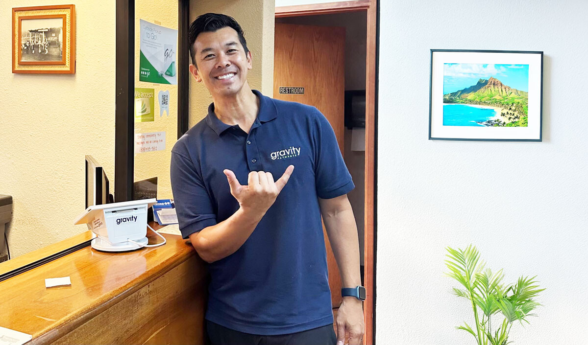 Micah in Hawaii smiling next to a Clover Mini payment processing terminal